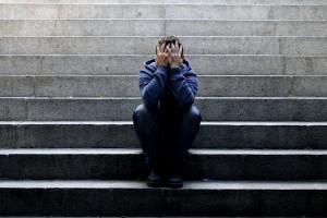 Young desperate man in casual clothes abandoned lost in depression sitting on ground street concrete stairs alone suffering emotional pain, sadness, looking sick in grunge lighting